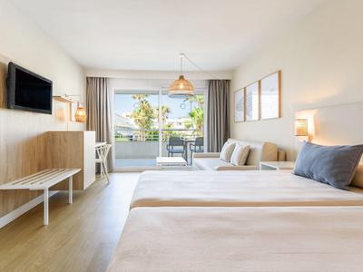 Helles, modernes Hotelzimmer mit zwei Betten, Sitzbereich, Wand-TV und großen Fenstern mit Terrasse.