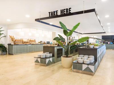 Moderner, heller Speisesaal mit Buffet, grünen Pflanzen und minimalistischer Einrichtung.