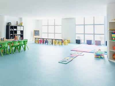 Heller, großer Gruppenraum mit bunten Kinderstühlen, Tischen und Spielmatten auf blauem Boden.