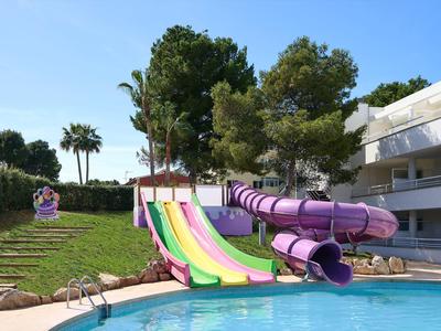 Buntes Schwimmbecken mit Rutschen und Wasserspielplatz, umgeben von Bäumen und Gebäuden.