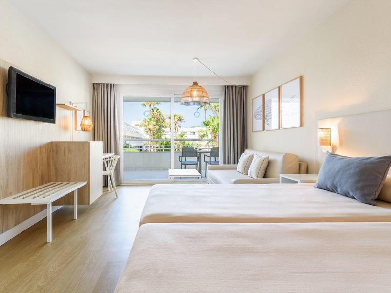 Camera d'albergo luminosa con due letti, balcone e vista su un giardino.