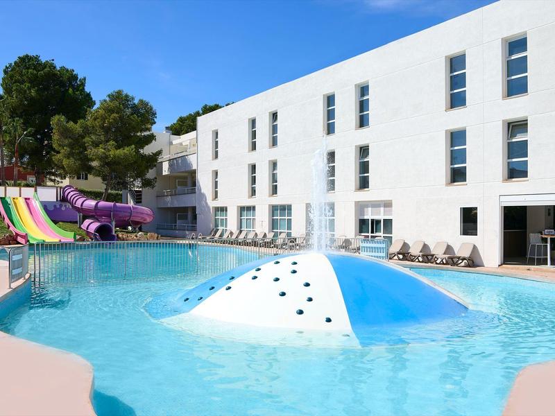 Piscina moderna con scivoli colorati e hotel bianco sullo sfondo.