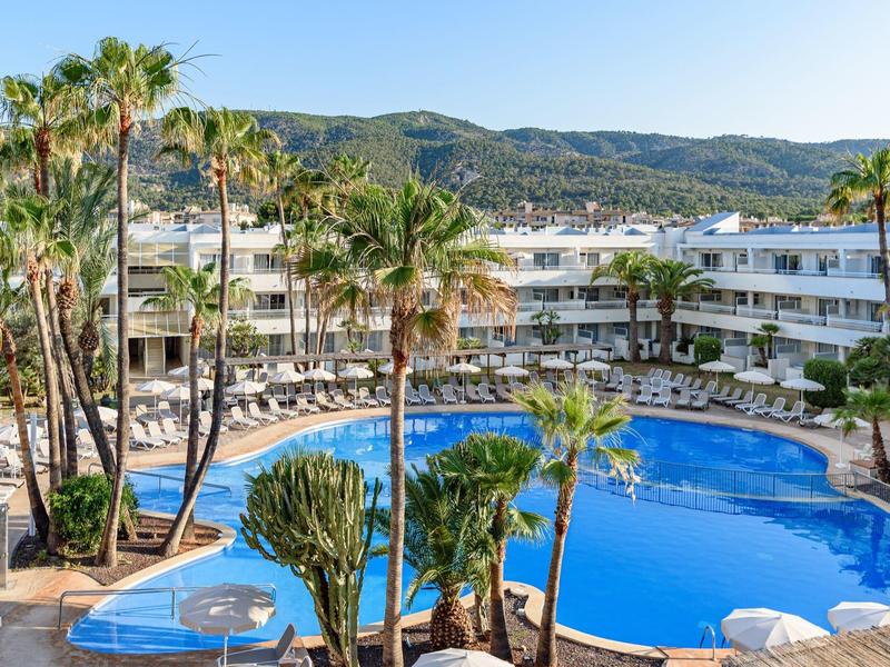 Piscina all'aperto circondata da palme e hotel moderno sullo sfondo.