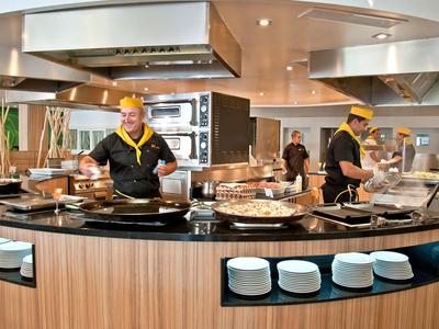 Modern hotel kitchen with cooking stations and staff in uniform preparing food.