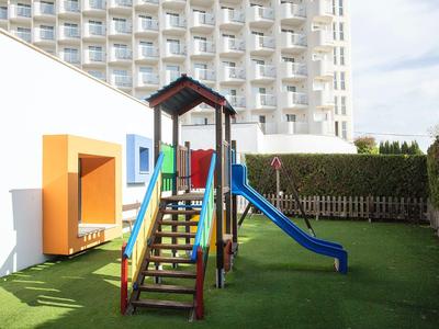 Small playground with slide and climbing frame in front of a hotel building with balconies