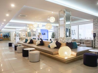 Hall di un hotel moderno con ampia area salotto, sgabelli rotondi e illuminazione decorativa.