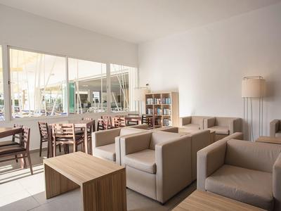 Bright lounge area with comfortable sofas, wooden tables, and chairs near large windows.