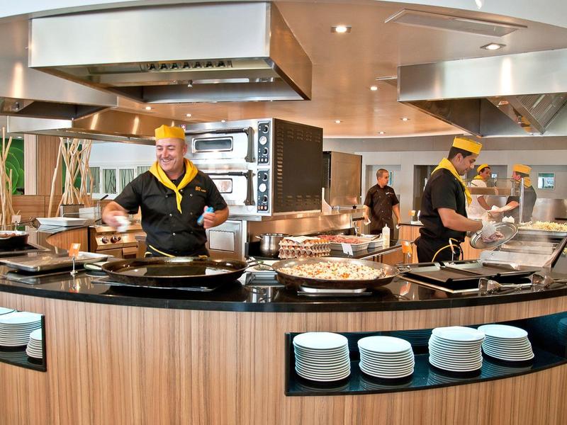 Modern hotel kitchen with cooking stations and staff in uniform preparing food.