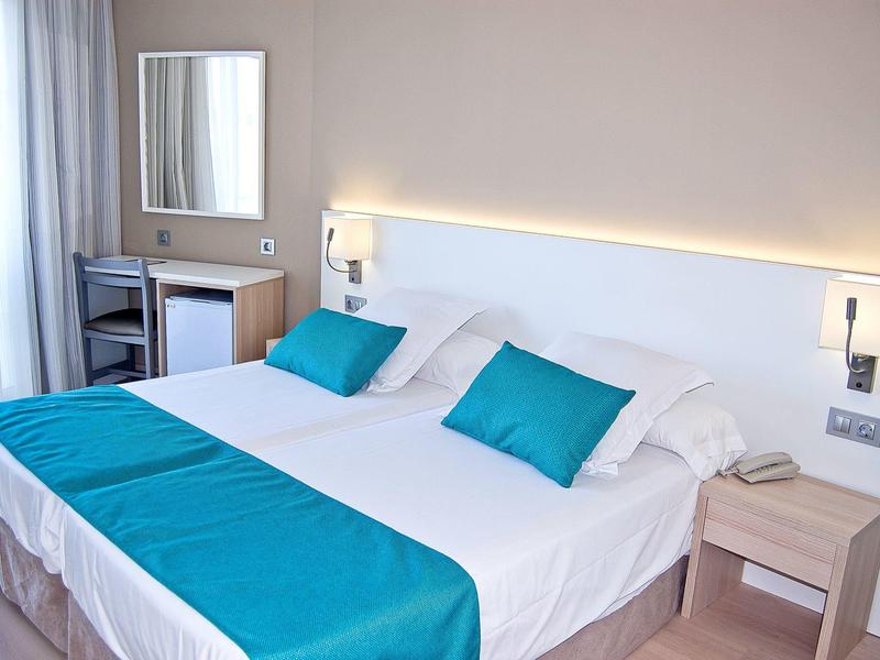 Modern hotel room with large double bed, white walls, and turquoise accents.