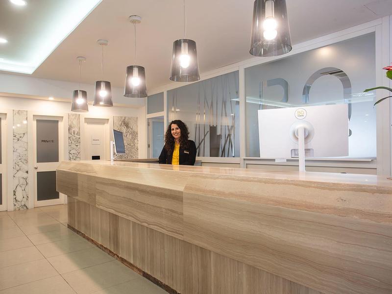 Modern hotel lobby with long wooden reception desk and receptionist.