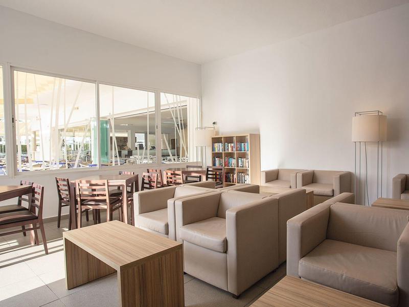 Bright lounge area with comfortable sofas, wooden tables, and chairs near large windows.