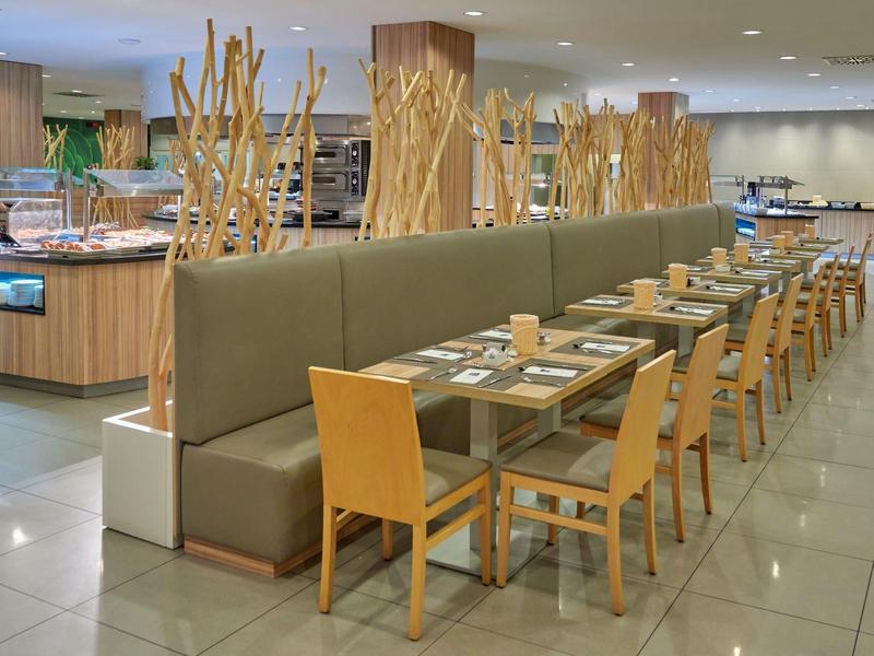 Modern hotel restaurant dining area with wooden furniture and decorative branches on light tiles.