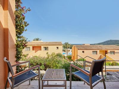 Balcon avec deux chaises et une table, vue sur des bâtiments et une montagne sous un ciel clair.