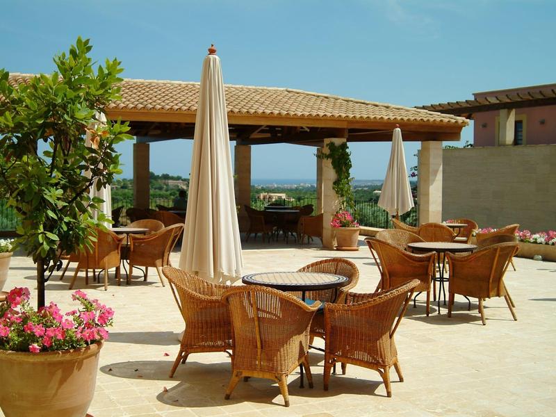 Terrasse ensoleillée avec tables, chaises et parasols fermés dans un hôtel.