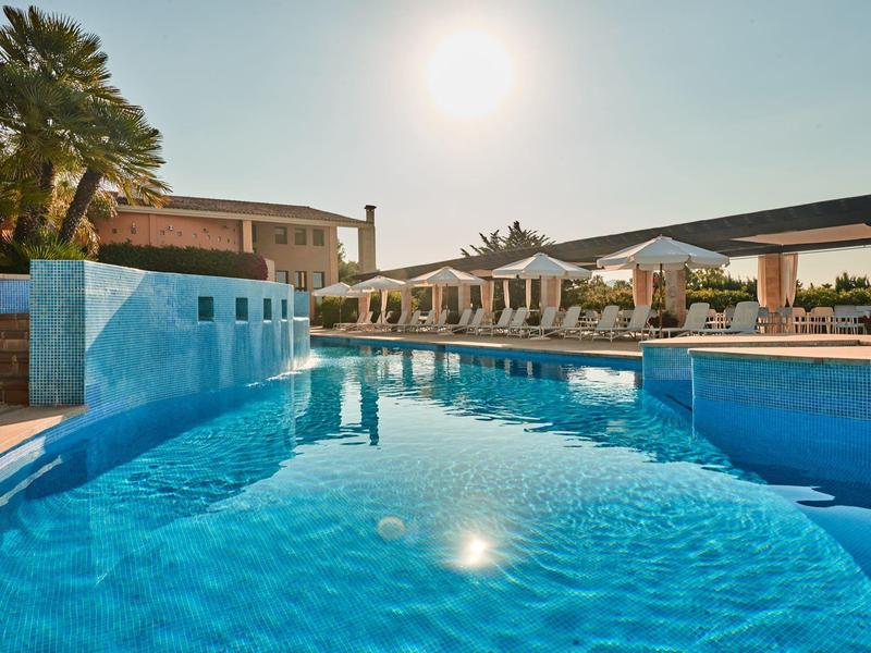 Espace piscine lumineux avec parasols et eau calme sous un ciel clair.