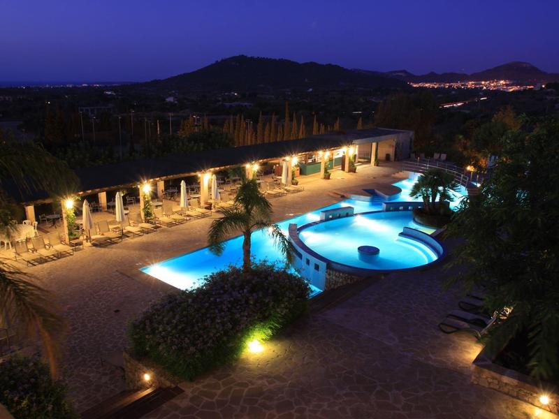 Vue nocturne de piscine illuminée et complexe hôtelier dans un paysage vallonné.