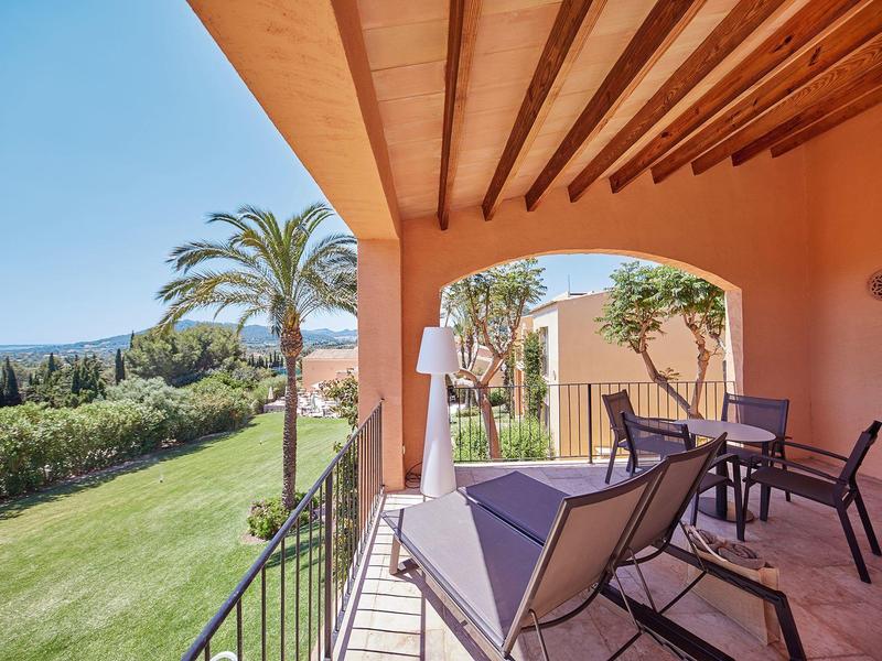 Balcon avec chaises et table donnant sur un jardin et des palmiers sous un ciel clair.