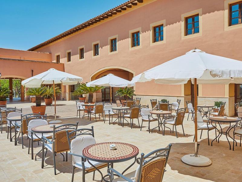 Terrasse extérieure ensoleillée avec tables et parasols devant un bâtiment d'hôtel.