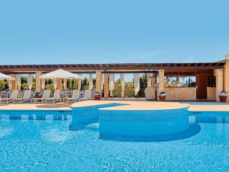 Piscine claire avec chaises longues et parasols sous un ciel bleu.