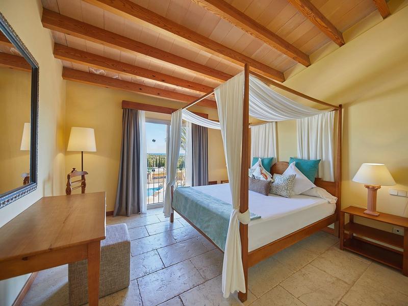 Chambre d'hôtel lumineuse avec lit à baldaquin, bureau, chaise et accès au balcon avec vue.