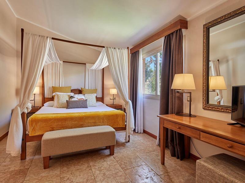 Chambre d'hôtel confortable avec lit à baldaquin, mobilier en bois et lumière naturelle chaleureuse.