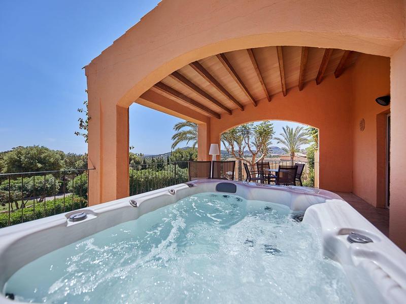 Jacuzzi extérieur sous une arche en terre cuite avec coin lounge et vue sur le jardin.
