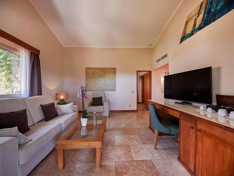 Chambre d'hôtel confortable avec canapé, TV, meubles en bois et grande fenêtre.