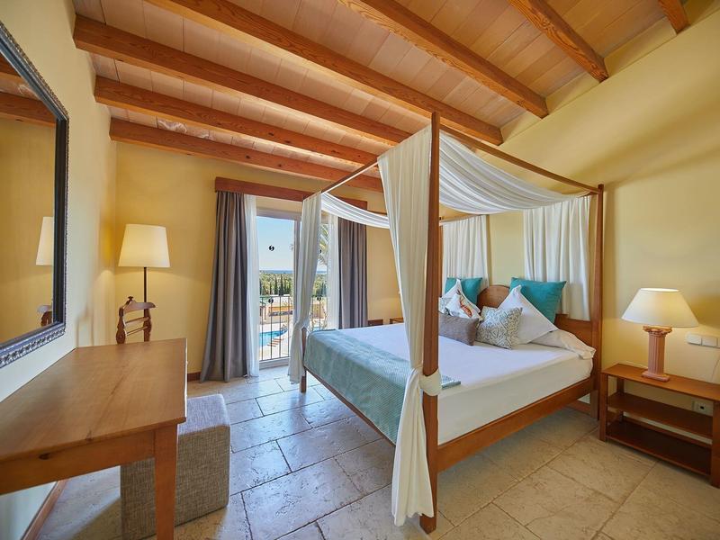 Chambre d'hôtel confortable avec lit à baldaquin, poutres en bois et balcon avec vue sur l'océan.