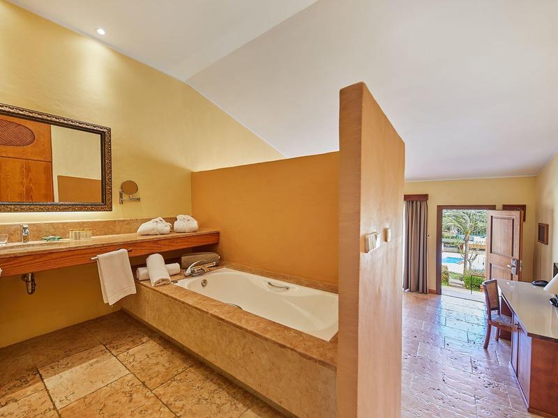 Chambre d'hôtel avec baignoire, lavabo et accès au balcon avec vue.