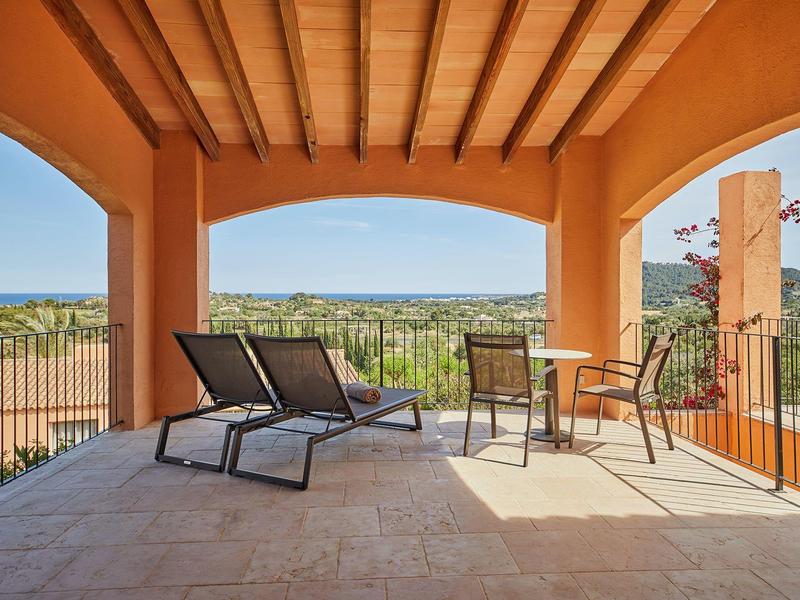 Terrasse avec chaises longues et table offrant une vue sur paysage ensoleillé et mer.