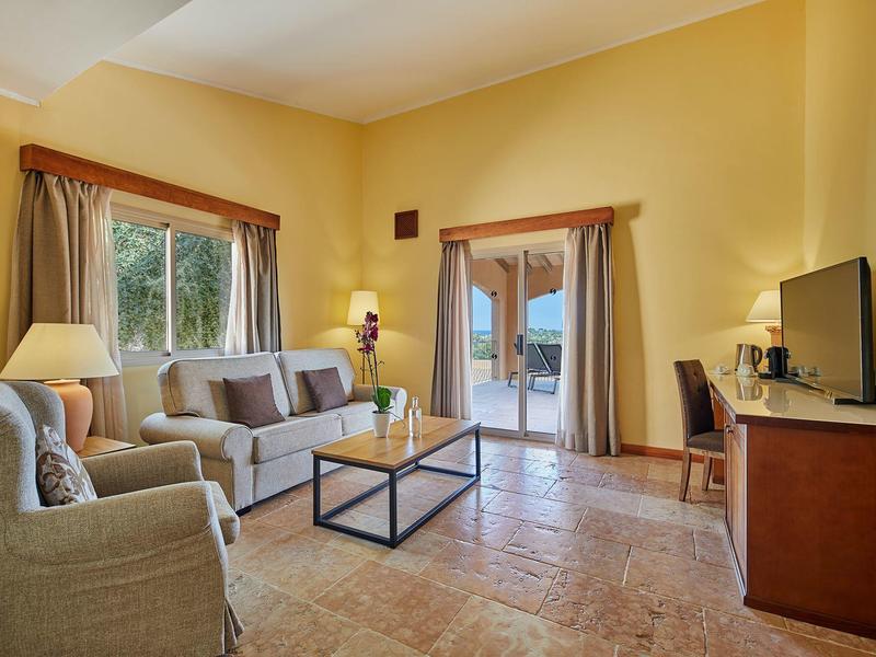 Salon confortable avec canapé, fauteuil, table basse et TV, donnant sur un balcon.