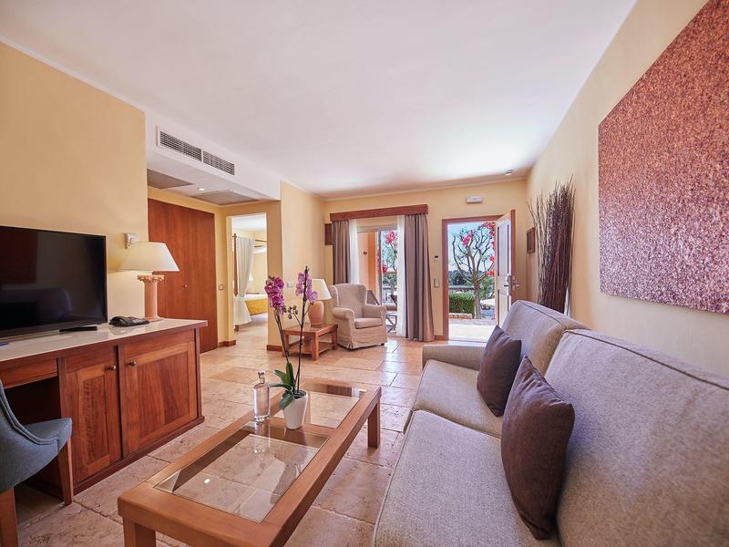 Suite d'hôtel lumineuse avec canapé, télévision, table basse et portes ouvertes sur un balcon.