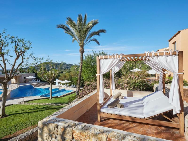 Lits de jour luxueux près de la piscine et des palmiers sous un ciel clair dans un complexe.