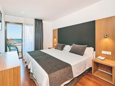Bright hotel room with double bed, wooden furniture, and balcony with sea view.