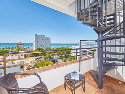 Balcony with chairs, table, and a view of the sea and surrounding buildings.
