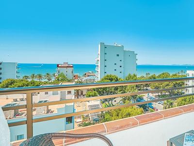 Balcony with chairs and table overlooking the sea under a blue sky.