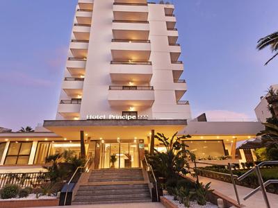 Modern hotel building with illuminated entrance and surrounding vegetation at dusk.