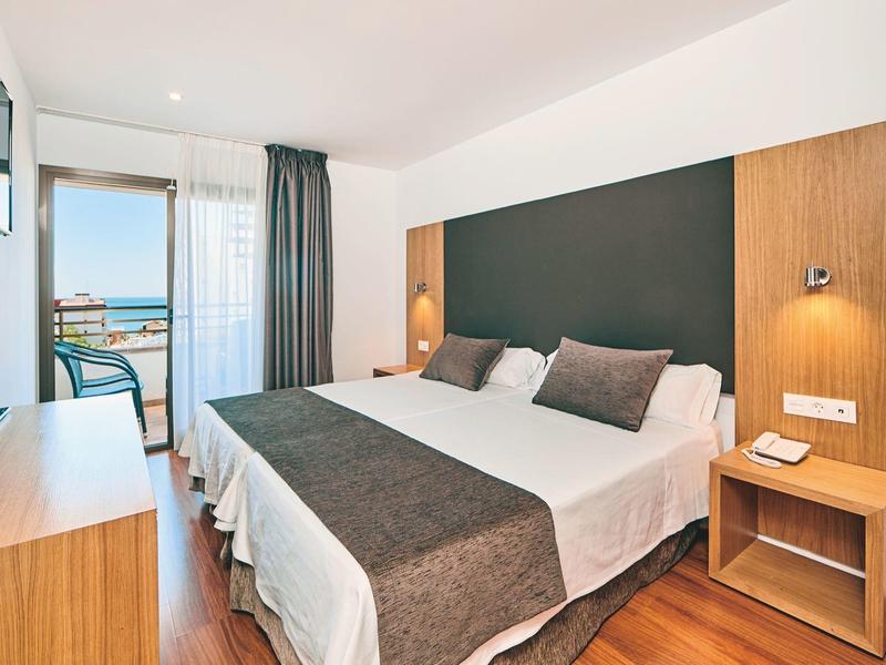 Bright hotel room with double bed, wooden furniture, and balcony with sea view.