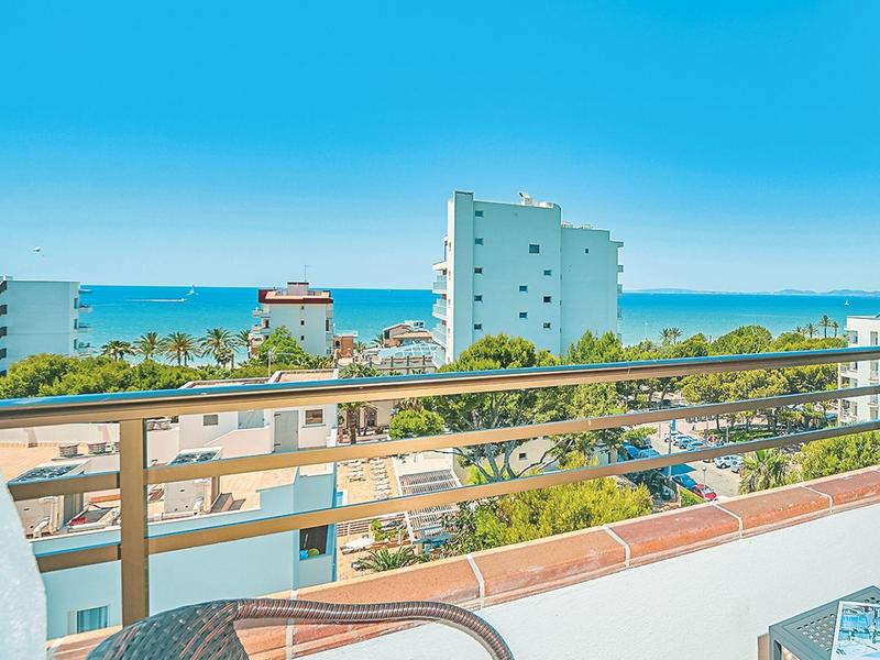 Balcony with chairs and table overlooking the sea under a blue sky.