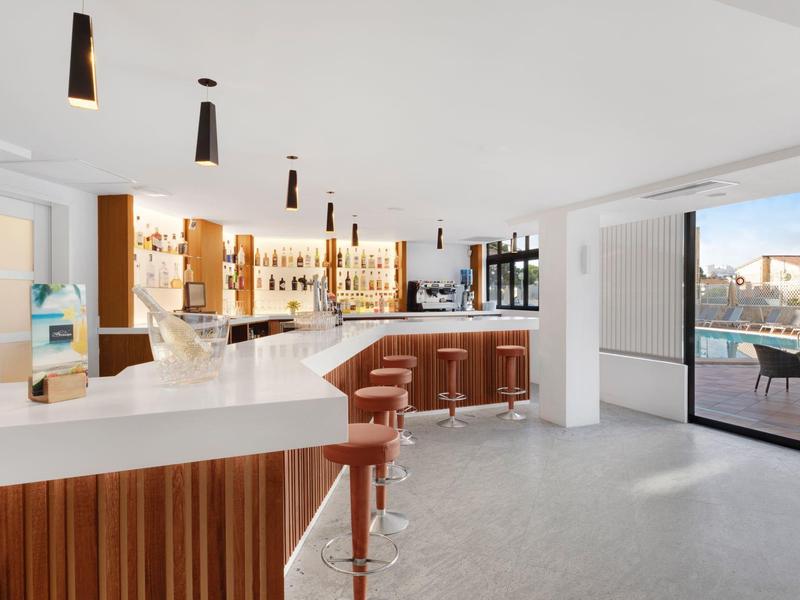 Modern hotel bar area with white counters, brown bar stools, and large window overlooking terrace.