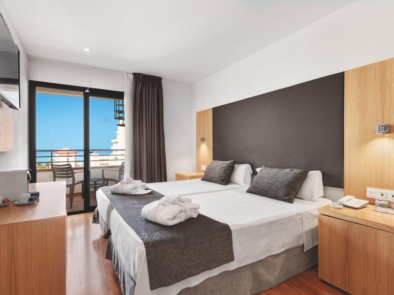 Modern hotel room with double bed, nightstands, and balcony with sea view.