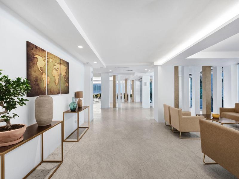 Modern hotel lobby with armchairs, plants, and abstract art on the wall.