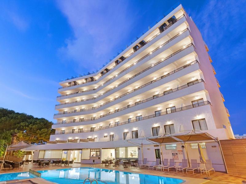 Modern hotel with illuminated pool at dusk and hills in the background