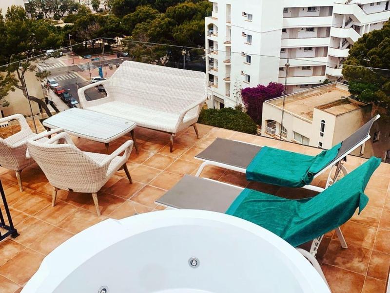 Balcony with hot tub, seating area, and view of residential buildings and sea in the background.