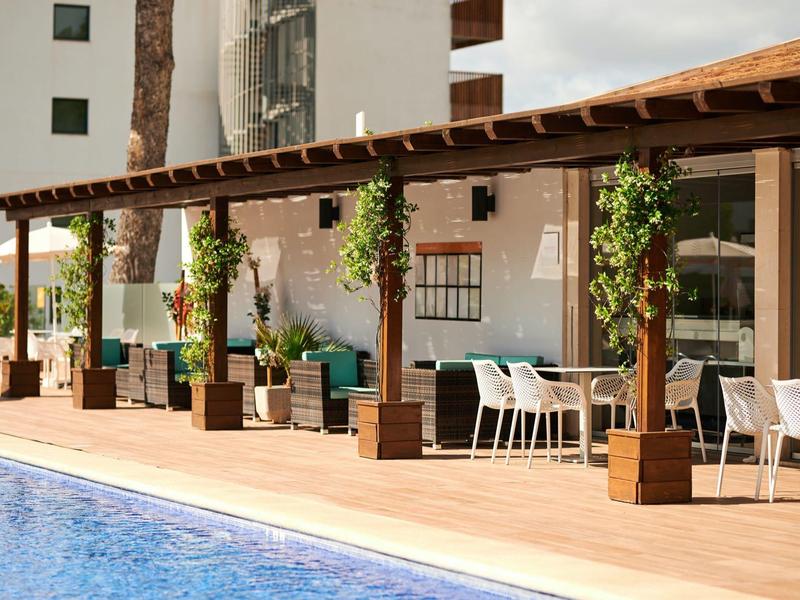 Strefa odpoczynku przy basenie z drewnianą pergolą i pnączami.