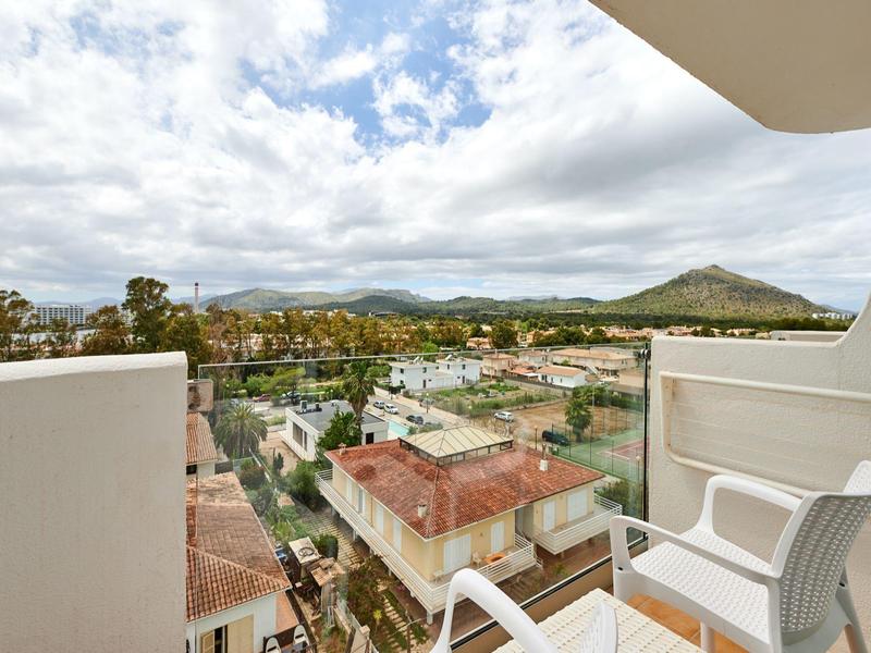 Balkon z krzesłami z widokiem na domy, zieleń i odległe wzgórza pod pochmurnym niebem.