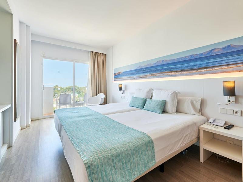 Jasny pokój hotelowy z dużym łóżkiem, jasnoniebieskimi akcentami i widokiem na morze