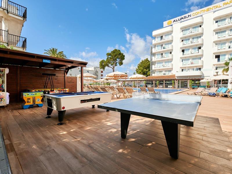 Zewnętrzny teren rekreacyjny z stołem do tenisa stołowego i piłkarzykami obok basenu i hotelu.