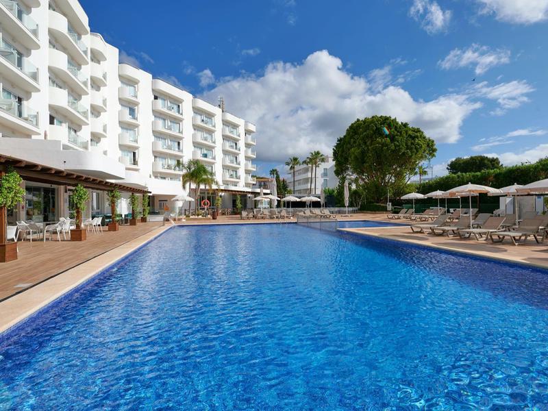 Basen na zewnątrz z leżakami i parasolami obok białego hotelu pod niebieskim niebem