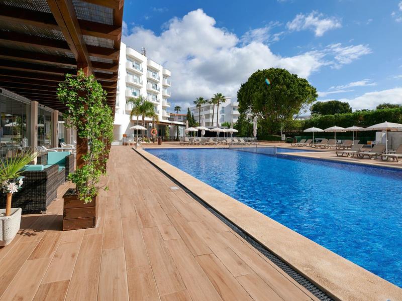 Basen na zewnątrz hotelu z drewnianym tarasem, leżakami, parasolami i niebieskim niebem.